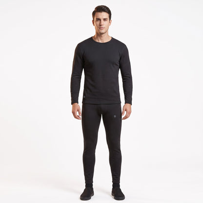 Full-body front view of a male model wearing a matching two-piece black smart heated thermal underwear set. The crew neck top has two black control icons at the hem, paired with full-length leggings against a solid white background.