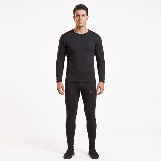 Full-body front view of a male model wearing a matching two-piece black smart heated thermal underwear set. The crew neck top has two black control icons at the hem, paired with full-length leggings against a solid white background.