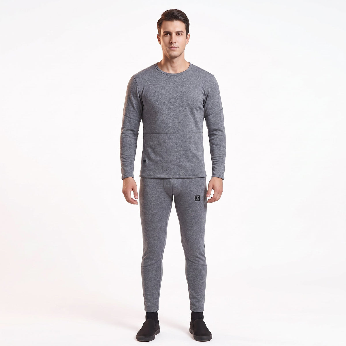 Full-body front view of a male model wearing a matching two-piece gray smart heated thermal underwear set. The crew neck top has two black control icons at the hem, paired with full-length leggings against a solid white background.