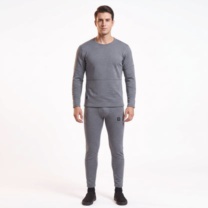 Full-body front view of a male model wearing a matching two-piece gray smart heated thermal underwear set. The crew neck top has two black control icons at the hem, paired with full-length leggings against a solid white background.